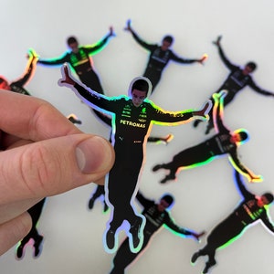 May include: A set of iridescent holographic stickers featuring a Formula 1 driver in a racing pose. The stickers feature the driver's name and the team logo, Petronas.