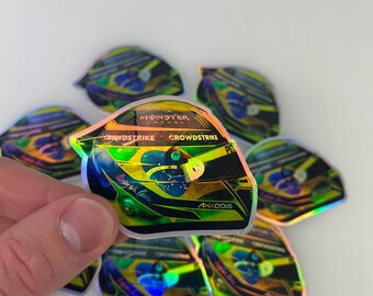 May include: A set of seven iridescent holographic stickers featuring a Formula One racing helmet with the logos "Monster Energy", "Crowdstrike", and "Akkodis".
