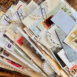 May include: A collection of vintage ephemera including aged paper, postcards, postage stamps, tickets, and black and white photographs. The items are layered and secured with gold-toned paper clips and white paper doilies inside a clear plastic sleeve.