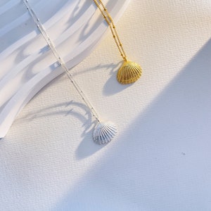 May include: Two delicate necklaces with shell pendants. The necklace on the left has a silver shell pendant, while the necklace on the right has a gold shell pendant.