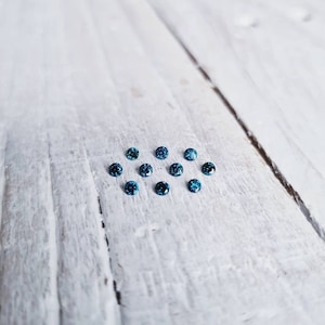 May include: A group of small, round, blue gemstones arranged in a loose circle on a white wooden surface.