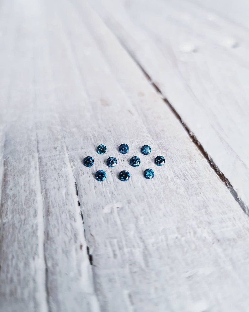 May include: A group of small, round, blue gemstones arranged in a loose circle on a white wooden surface.