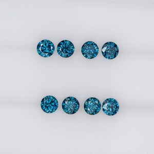 May include: Eight round blue gemstones, likely diamonds, arranged in two rows of four on a white surface.