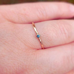 May include: A dainty gold ring with a tiny blue gemstone set in the centre.