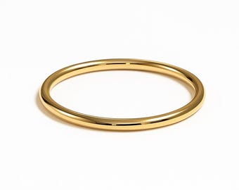 Puede incluir: Un brazalete dorado. El brazalete tiene un diseño circular simple con una superficie lisa y pulida. El brazalete es una banda sólida y sin costuras, que refleja la luz sobre un fondo blanco. Una pieza de joyería clásica.