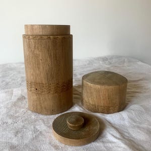 Op de afbeelding: Een houten container met een deksel en een aparte bovenkant. De container is gemaakt van lichtbruin hout en heeft een eenvoudig, rustiek ontwerp.