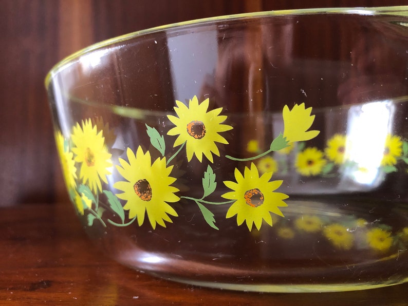 May include: A clear glass baking dish with a yellow and green sunflower design.