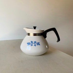 May include: White enamel teapot with a blue floral design and a black handle. The teapot has a silver lid with a black knob.