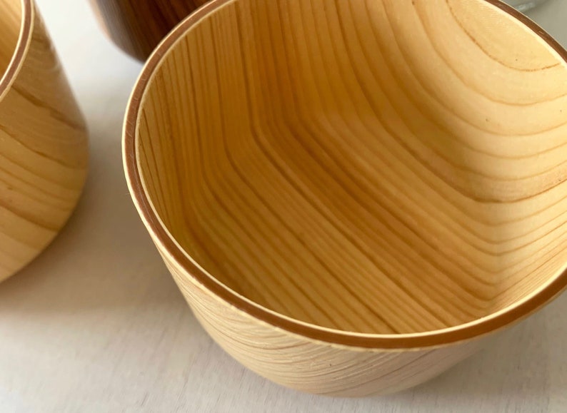 May include: A wooden bowl with a natural wood finish. The bowl has a smooth, rounded interior and a slightly flared rim.