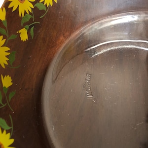 May include: A brown glass serving bowl with a floral design featuring yellow sunflowers and green leaves. The bowl is marked with the word "Borgonovo" on the bottom.