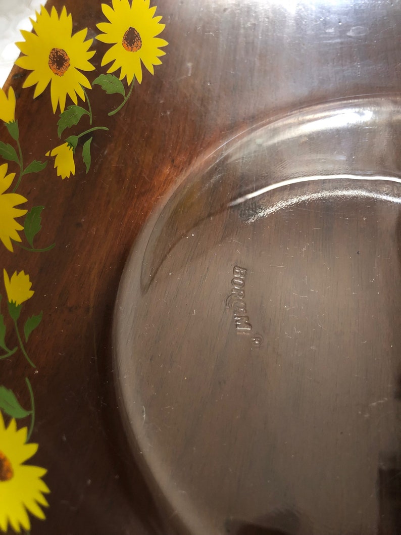 May include: A brown glass serving bowl with a floral design featuring yellow sunflowers and green leaves. The bowl is marked with the word "Borgonovo" on the bottom.