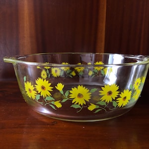 May include: A clear glass baking dish with a yellow and green floral design. The design features a repeating pattern of sunflowers with green leaves.