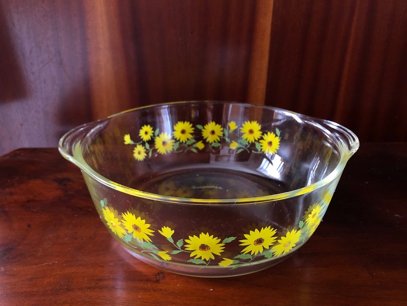 May include: A clear glass baking dish with yellow and green floral design. The dish has two handles on the sides.