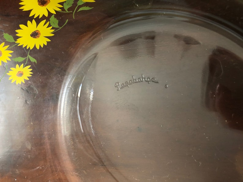 May include: A clear glass baking dish with a brown rim and a sunflower design. The bottom of the dish is marked with the word "Pyrex".