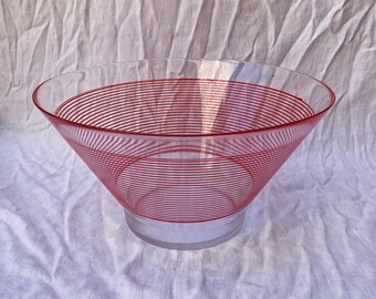 Könnte beinhalten: Eine klare Glasschüssel mit einem roten konzentrischen Kreisdesign. Die Schüssel steht auf einem weißen Stoffhintergrund.