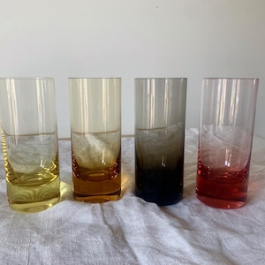 Può includere: Quattro bicchieri di vetro trasparente con liquido di diversi colori al loro interno. I bicchieri sono allineati in una fila su una superficie bianca. Il liquido nei bicchieri è giallo, arancione, grigio e rosso.