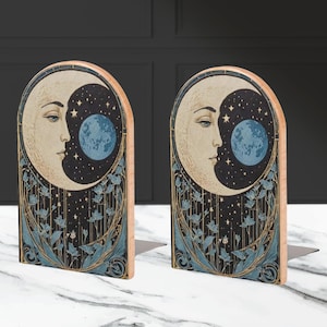 May include: A pair of wooden bookends featuring a crescent moon with a face and a blue orb, surrounded by stylized flowers and stars on a black background.