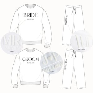 K&ouml;nnte beinhalten: Wei&szlig;er Pullover mit "BRIDE" und "EST. 2024" aufgedruckt auf der Vorderseite. Wei&szlig;e Jogginghose mit "WILLIAMS" aufgedruckt an der Seite. Nahaufnahme eines wei&szlig;en gestickten "MR" auf der Brust des Pullovers. Nahaufnahme eines wei&szlig;en gestickten "J & P" mit einem Herzen am &Auml;rmel des Pullovers.