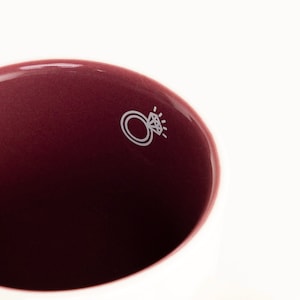 May include: A close-up of the inside of a burgundy ceramic mug with a white ring and diamond design.