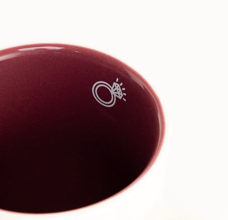 May include: A close-up of the inside of a burgundy ceramic mug with a white ring and diamond design.