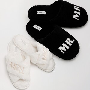 May include: A pair of white fuzzy slippers with the word "MRS." embroidered on them and a pair of black fuzzy slippers with the word "MR." embroidered on them.