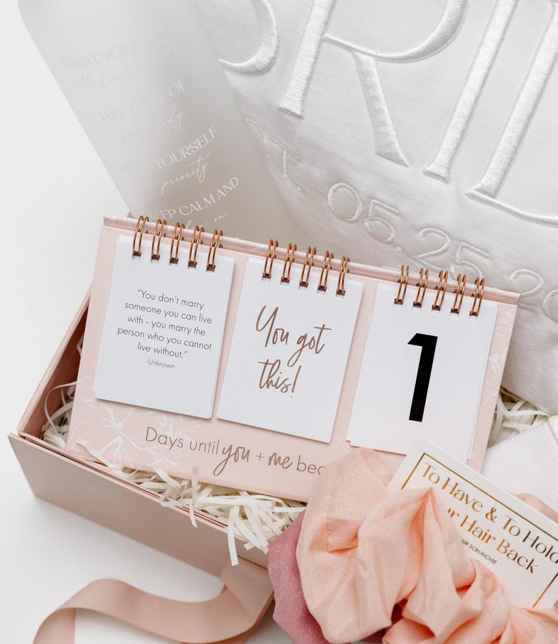 以下が含まれることがあります： ピンク色のギフトボックスには、「Days until you + me bec」のテキストが入ったカウントダウンカレンダーが入っています。 カレンダーには「You got this!」という言葉と数字「1」が書かれた3ページがあります。 また、シュシュと装飾枕も含まれています。
