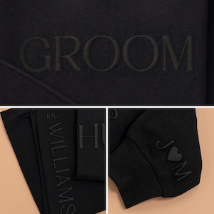 K&ouml;nnte beinhalten: Schwarzer Pullover mit dem Wort "GROOM" auf der Vorderseite gestickt. Der linke &Auml;rmel ist vertikal mit dem Text "MR. WILLIAMS" bestickt. Der rechte &Auml;rmel ist mit einem Herzen mit den Buchstaben "JM" bestickt.