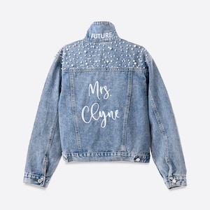 Personalized bridal denim jacket. Made from soft denim and decorated with faux pearls for a chic look. White jean jacket custom embroidered with your name. Perfect to wear for an engagement photoshoot.
