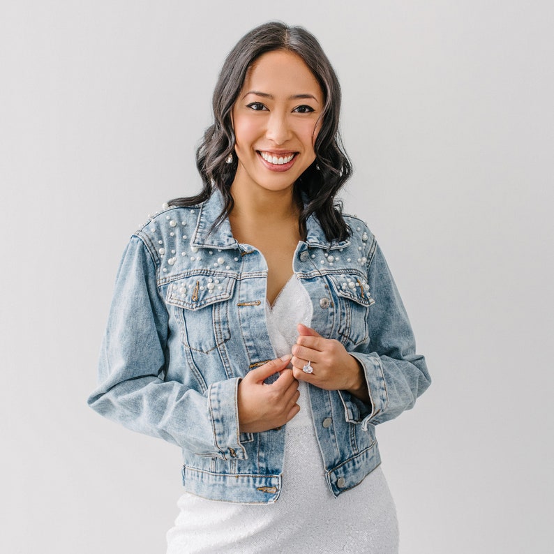 Personalized bridal denim jacket. Made from soft denim and decorated with faux pearls for a chic look. White jean jacket custom embroidered with your name. Perfect to wear for an engagement photoshoot.