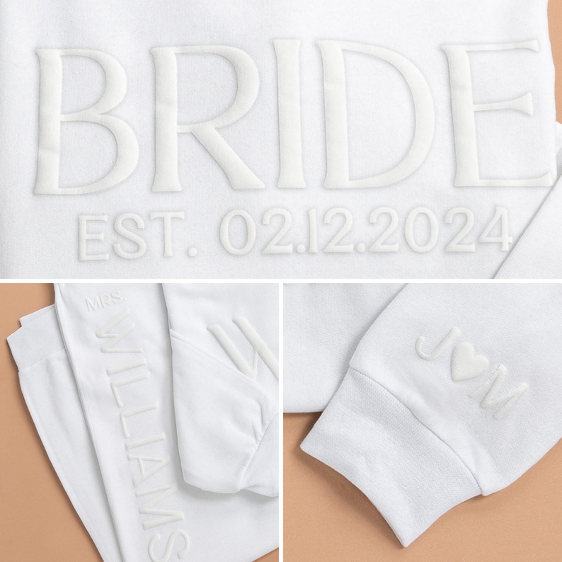 K&ouml;nnte beinhalten: Wei&szlig;er Pullover mit dem Wort "BRIDE" in erhabener Schrift und dem Text "EST. 02.12.2024". Der Pullover hat auch den Text "MRS. WILLIAMS" auf dem linken &Auml;rmel und "J & M" mit einem Herzen auf dem rechten &Auml;rmel.