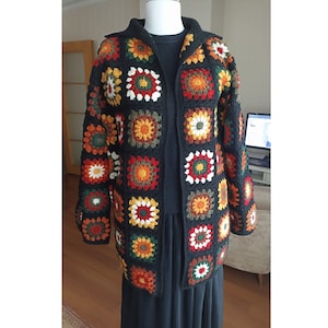 May include: A black crochet cardigan with a colorful geometric pattern. The cardigan has a long, open front and is made of a soft, lightweight yarn.