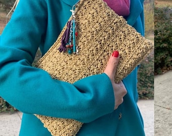 May include: A beige crocheted clutch with a starburst pattern. The clutch has a decorative tassel with beads and a silver clasp. The person is wearing a teal coat and a pink scarf.