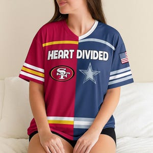 May include: A split-design t-shirt with the text "HEART DIVIDED". The left side is burgundy with gold and white stripes and a San Francisco 49ers logo. The right side is navy blue with a Dallas Cowboys star and an American flag.