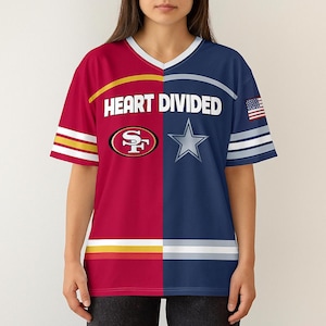 May include: A v-neck t-shirt with a split design featuring the San Francisco 49ers and Dallas Cowboys logos. The shirt is red and navy blue, with the text "HEART DIVIDED" across the chest. An American flag is on the sleeve.