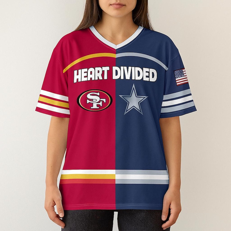 May include: A v-neck t-shirt with a split design featuring the San Francisco 49ers and Dallas Cowboys logos. The shirt is red and navy blue, with the text "HEART DIVIDED" across the chest. An American flag is on the sleeve.
