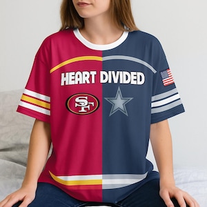 May include: A split-design t-shirt with the text "HEART DIVIDED". One side is red with a gold and white stripe, the other is navy blue with a white star and an American flag. The shirt features the logos of the San Francisco 49ers and the Dallas Cowboys.