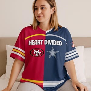 May include: A short-sleeved t-shirt with a split design. One side is red with the San Francisco 49ers logo, and the other is navy blue with the Dallas Cowboys star logo. The shirt has the text "HEART DIVIDED" across the chest.