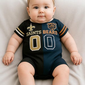May include: A baby wearing a black and navy blue football-style onesie with the words "SAINTS BEARS" and the number "00". The onesie has gold and orange accents. The baby is also wearing a beige bow headband.