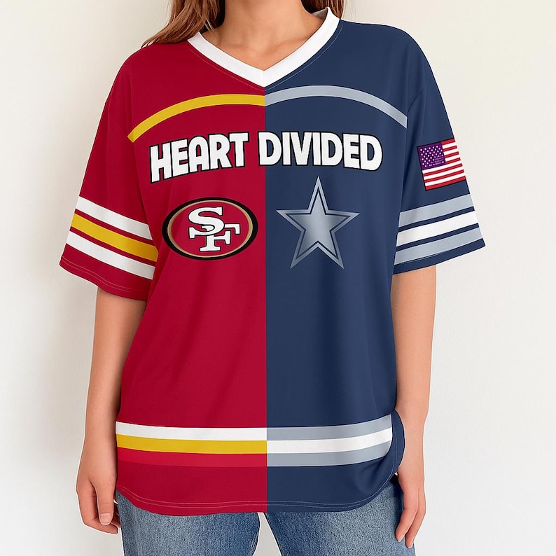 May include: A red and navy blue short-sleeved t-shirt with a split design. The left side features the San Francisco 49ers logo, while the right side displays a Dallas Cowboys star. The text "HEART DIVIDED" is across the chest, with an American flag on the sleeve.