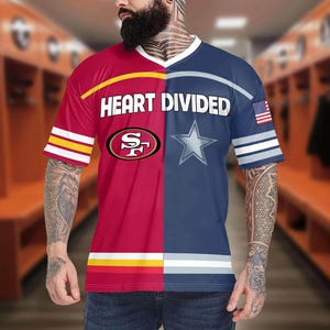 May include: A short-sleeved t-shirt with a split design. One side is red with a yellow stripe and the San Francisco 49ers logo. The other side is navy blue with a white star and an American flag patch. The text "HEART DIVIDED" is across the chest.
