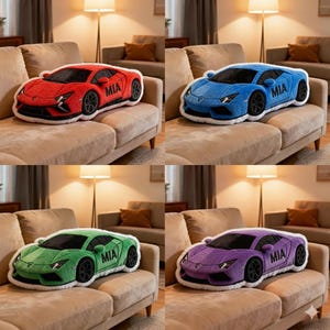 May include: Four plush car-shaped pillows in red, blue, green, and purple, each with black wheels and a white trim. The text "MIA" is on the side of each car. The pillows are displayed on a beige sofa.