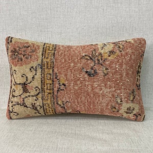 Może przedstawiać: Prostokątna poduszka z różowo-beżowym wzorem kwiatowym. Poduszka ma frędzlowaną krawędź i jest wykonana z miękkiej, tkanej tkaniny.