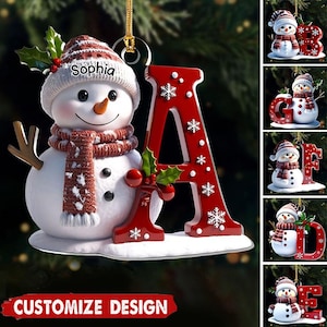 May include: A snowman Christmas ornament with a red letter "A" and the name "Sophia". The snowman wears a striped hat and scarf. The letter "A" is red with white snowflakes and holly accents. The words "CUSTOMIZE DESIGN" are at the bottom.
