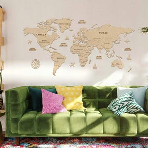 Könnte beinhalten: Ein grünes Samtsofa mit einer Weltkarte aus Holz an der Wand dahinter. Das Sofa hat mehrere bunte Kissen und steht in einem Wohnzimmer mit einem Holzregalbrett und einer Topfpflanze.