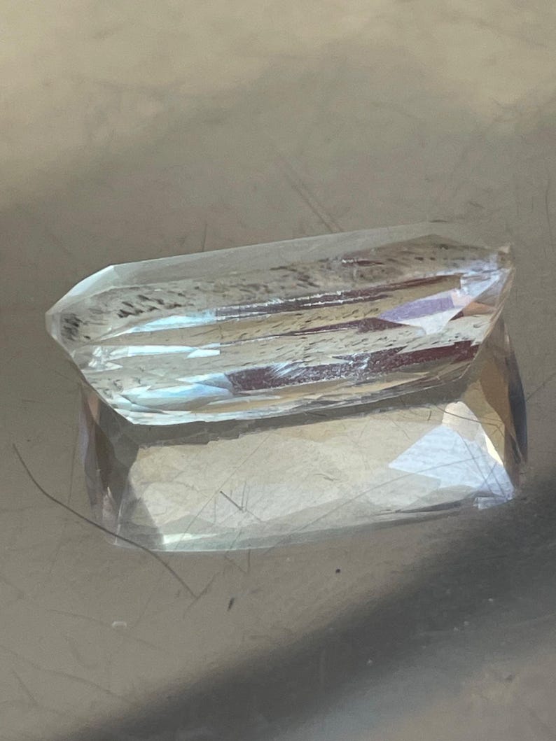 K&ouml;nnte beinhalten: Ein klarer, facettierter Edelstein mit rechteckiger Form. Der Edelstein hat mehrere Facetten, die das Licht reflektieren und einen funkelnden Effekt erzeugen. Der Edelstein ist wahrscheinlich ein Kristall oder ein geschliffenes Glasst&uuml;ck.