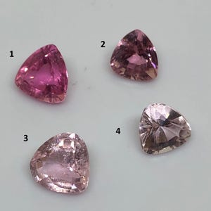 Może przedstawiać: Wyświetlane są cztery trójkątne kamienie szlachetne w odcieniach różu i brzoskwini. Kamienie szlachetne są fasetowane, o różnym stopniu przezroczystości i nasycenia koloru. Kamienie są ułożone na jasnym tle.