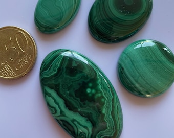 May include: Five polished malachite stones in various oval and round shapes. The stones display a rich, swirling pattern of dark and light green hues. A 50 Euro cent coin is next to the stones for size comparison.