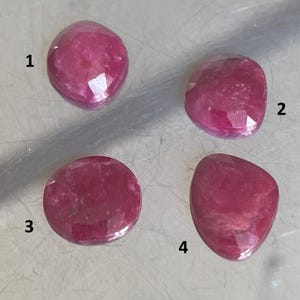 May include: Four faceted, oval-shaped, and round ruby gemstones. The gemstones are a deep, rich red color, with variations in shape and cut. The gemstones are numbered 1 through 4.