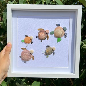 May include: A framed artwork featuring five sea turtle designs made from seashells and sea glass. The turtles are arranged in a row on a white background.