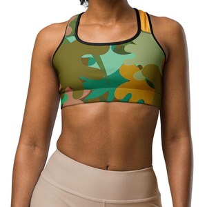 Könnte beinhalten: Ein Sport-BH mit einem abstrakten Muster in Grün, Gelb und Blau. Der BH hat ein schwarzes Band um die Brust und dünne Träger.